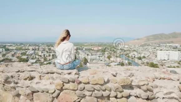 神秘的女人一头鲜艳的飞染头发坐在岩石上的石船边上欣赏第比利斯的风景如画视频的预览图