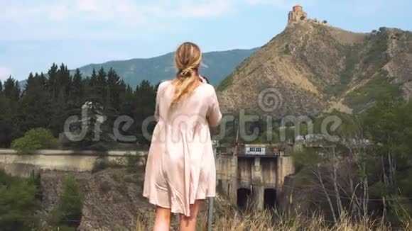 专业摄影师年轻的金发女郎穿着浅粉色的夏季飞行服装女士为格鲁吉亚人拍照视频的预览图