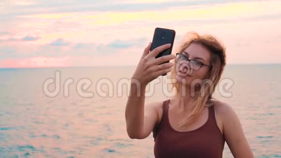 美丽的年轻女士在大海和五彩缤纷的天空前在格鲁吉亚日落女孩博主自拍视频的预览图