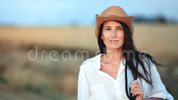 漂亮的背包客戴着帽子的女性在麦田里摆姿势看着镜头视频的预览图