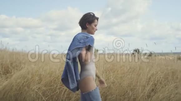 一位穿着紧身衣短发肩上夹着牛仔裤夹克的迷人女人的侧面景色视频的预览图