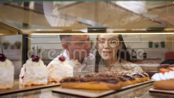 快乐的一对夫妇在玻璃橱窗里挑选美味的蛋糕视频的预览图
