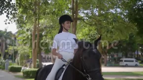 阳光明媚的一天美丽的亚洲女孩戴着黑色头盔和白色T恤在公园里骑马这是大自然放松的好方式视频的预览图