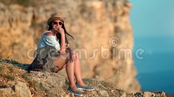 迷人的旅游女性在日落时分坐在山顶上享受休息视频的预览图