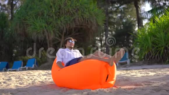 热带海滩上的年轻人躺在充气沙发上他刚刚充气暑假概念视频的预览图