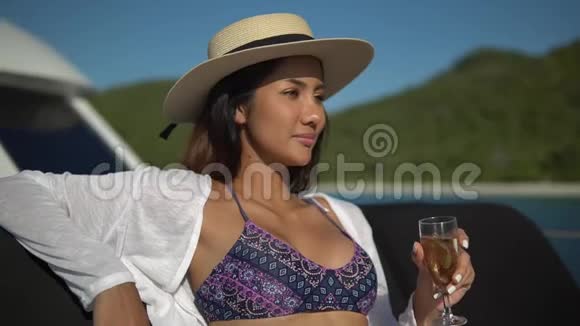 一位年轻的黑发女郎穿着白色衬衫戴着一顶灰帽子坐在沙发上坐在优秀的游艇上慢悠悠地喝着香槟视频的预览图