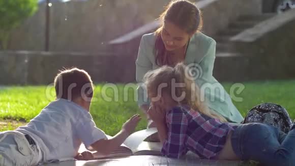 孩子的成长年轻的女人在阳光下为坐在绿色草坪上的孩子阅读有趣的书视频的预览图