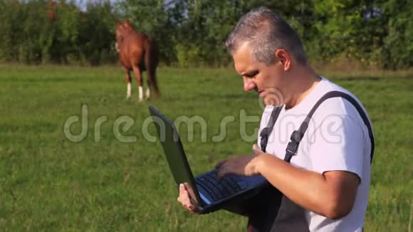 农夫在马附近使用笔记本电脑视频的预览图