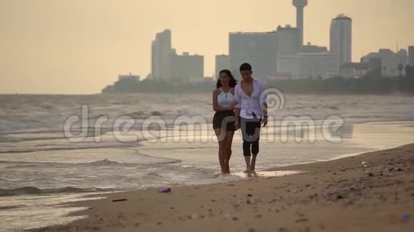 年轻的男女赤着脚携手走在沙滩上慢动作的女孩和她的男朋友在一起视频的预览图
