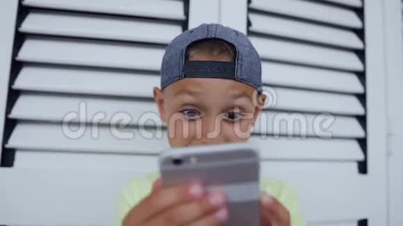 小男孩在玩网络游戏时使用手机的特写有趣可爱的孩子在智能手机上玩游戏小可爱视频的预览图