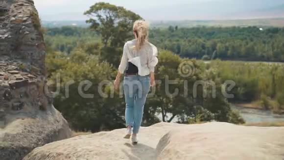 穿着宽松衣服的可爱苗条的年轻女子正慢慢地沿着口袋爬上悬崖走向壮丽的山崖视频的预览图