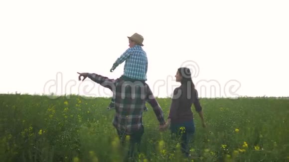 农业年轻男子肩上扛着小男孩女孩子在绿油油的油菜田里迎着明亮的天空散步视频的预览图