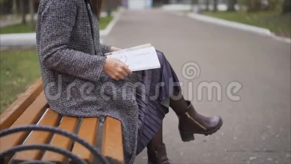秋天的城市里年轻漂亮的商业女人坐在长凳上秋天美丽的女孩坐在长凳上树叶上视频的预览图
