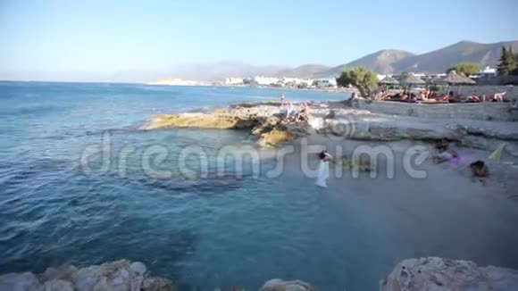 美丽的黑发女人穿着白色的裙子站在海滨享受海风和大海视频的预览图