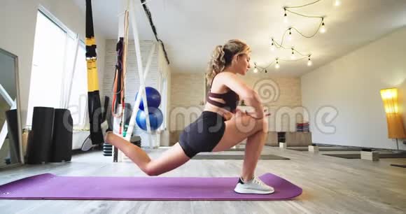 在一个现代设备齐全的瑜伽工作室里女士一边穿着运动垫一边用弹性支撑伸展双腿视频的预览图