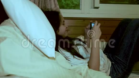 吐温女孩躺在床上玩智能手机视频的预览图