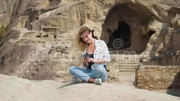 一个金发碧眼的年轻女子天生丽质坐在石头上的莲花位置在手机上输入一条信息这就是视频的预览图