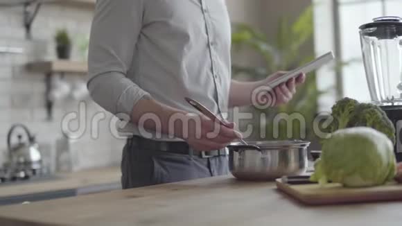 不可辨认的男人在衬衫上煮汤检查食谱在厨房里的平板电脑上健康观念视频的预览图