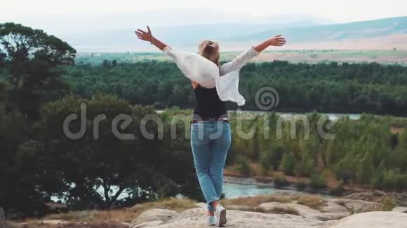 一个甜美苗条的年轻女子站在悬崖上双臂向上举视频的预览图