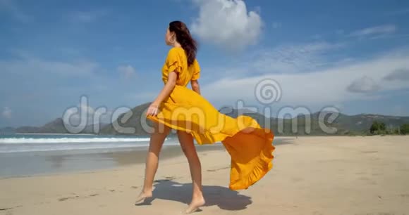 美丽的赤脚小姐走在阳光明媚的海滩上黄色的连衣裙随风飘扬是散步的好日子视频的预览图