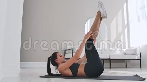 抬起身体进行腹肌锻炼双腿在平坦的光线下抬起女人在家里训练视频的预览图