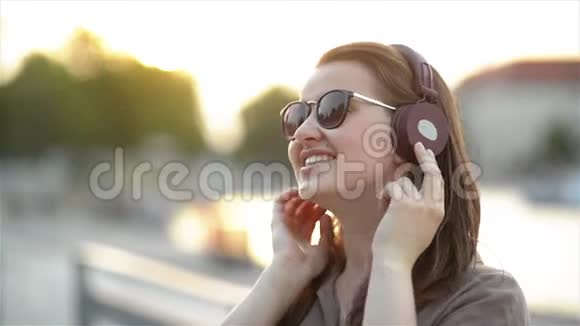 特写年轻漂亮女孩在大耳机上听音乐戴可爱太阳镜在城市唱歌的滑稽画像视频的预览图