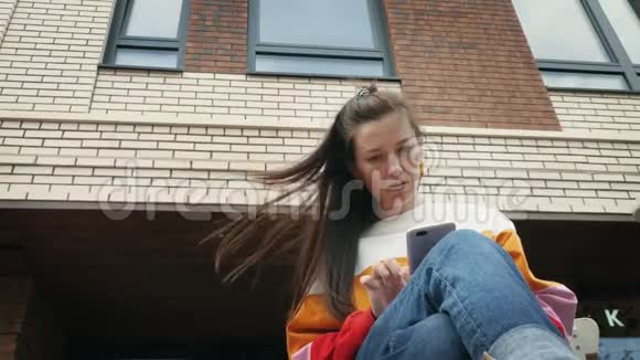 年轻的美女在砖楼附近使用智能手机视频的预览图