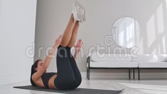 抬起身体进行腹肌锻炼双腿在平坦的光线下抬起女人在家里训练视频的预览图