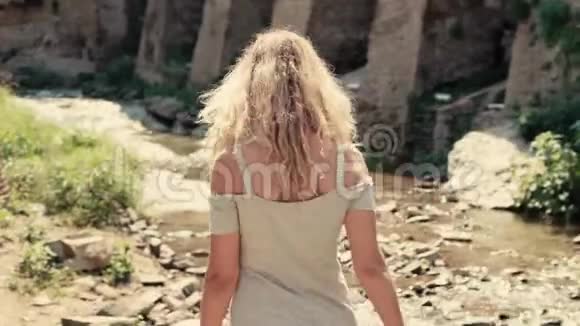 穿着灰色短裙的瘦小女子手里拿着电话走在小河边一位金发女郎视频的预览图