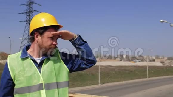 一个戴着黄色头盔的胡子和胡子的工人站在桥上望着远处他的手靠近他的h视频的预览图