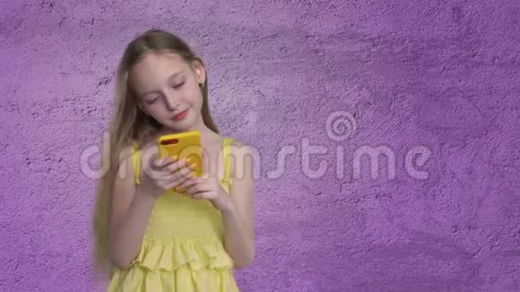 长发少女在紫罗兰墙背景上看手机美丽的女孩在风中挥舞着头发视频的预览图