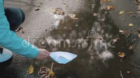 可爱的女孩在秋天公园的水坑里玩纸船童梦和旅行理念生活方式视频的预览图