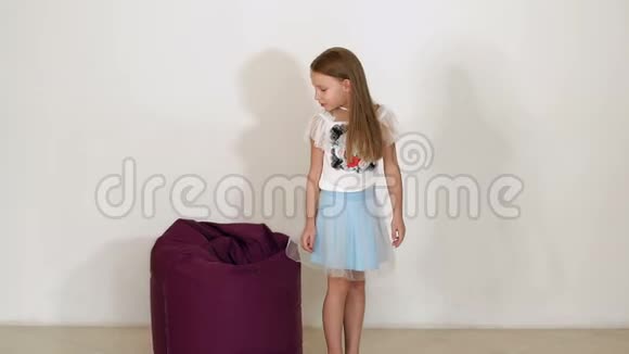 小女孩穿着蓬松的裙子倒在白色背景的紫豆袋沙发上视频的预览图