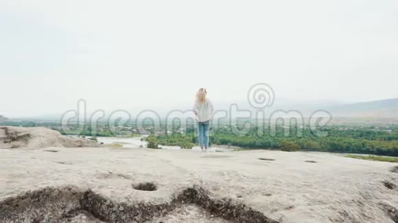 从悬崖边俯瞰格鲁吉亚壮丽的景色身穿鲜艳夏装的金发女孩站在山上视频的预览图