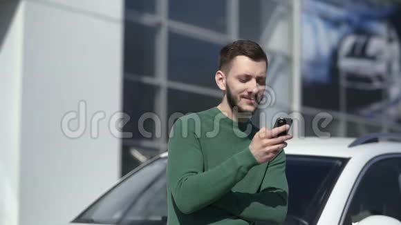 英俊男子使用智能手机并站在汽车附近的肖像视频的预览图