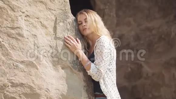 一个年轻的金发女人一张漂亮的脸靠在古城的岩石上女孩听着视频的预览图