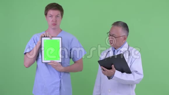成熟的日本男性医生带着年轻男性病人展示数字平板电脑解释一些事情视频的预览图