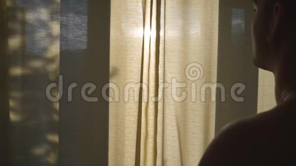 无法辨认的运动男在酒店的卧室拉开窗帘早上看着窗外年轻人视频的预览图