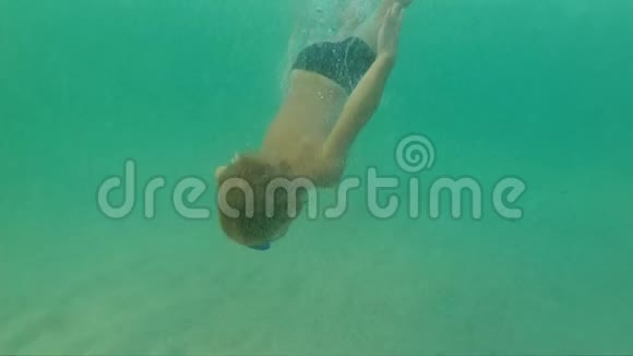 一个小男孩在蓝色的海洋中潜水并到达海底的超慢镜头视频的预览图