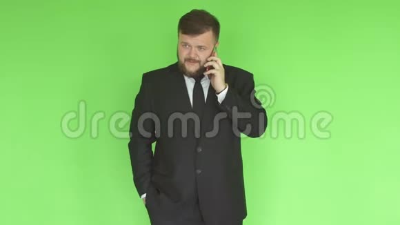 一名身穿黑色西装留着胡子的白人男子在绿墙背景下通过电话解决问题视频的预览图