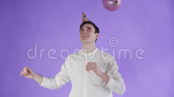 戴着派对帽的年轻人在紫色背景下的气球下跳舞视频的预览图