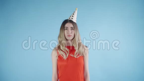戴着派对帽的漂亮女孩站在蓝色背景下的纸屑下视频的预览图