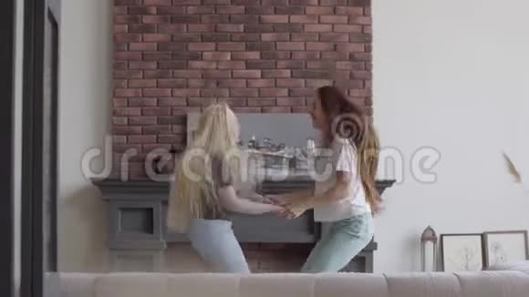两个金发黑发的小女孩在客厅里牵手跳跃布鲁内特女孩和白化病女孩视频的预览图