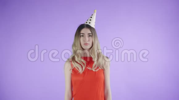 戴着派对帽的漂亮女孩站在紫色背景下的纸屑下视频的预览图