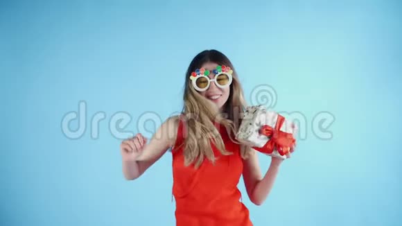 戴着滑稽眼镜手里拿着礼物的年轻女子正在蓝底跳舞视频的预览图