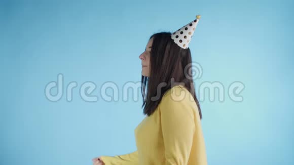 穿着黄色毛衣戴着派对帽的年轻女子正在蓝底跳舞视频的预览图