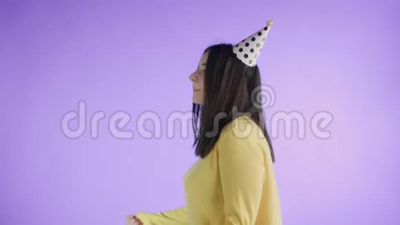穿着黄色毛衣戴着派对帽的年轻女子在紫色背景上跳舞视频的预览图