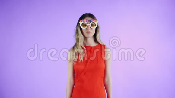 戴着滑稽眼镜的红色裙子的年轻女子正在紫色背景上跳舞视频的预览图