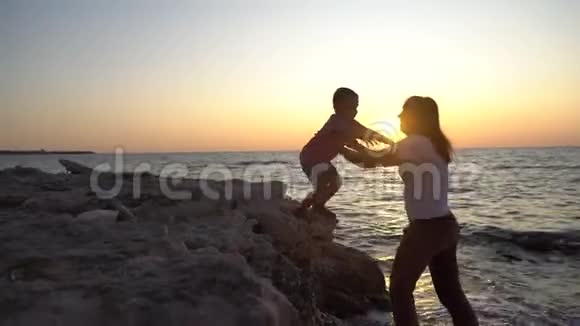 小男孩和他妈妈在海上日落背景下的剪影视频的预览图