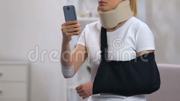 戴颈领和手臂吊带的悲伤女士在智能手机上打字车祸视频的预览图